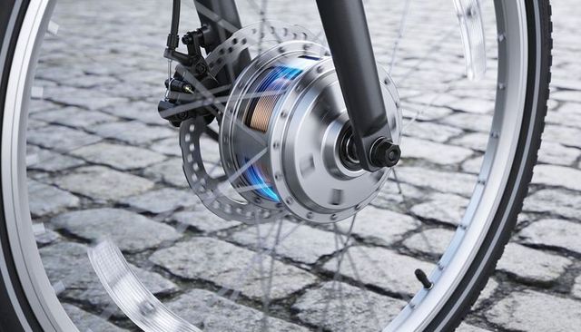 Front electric bike hub motor spinning on cobblestone with glowing copper windings and disc