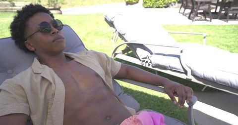 African american man relaxing on patio lounge chair wearing sunglasses and swim trunks
