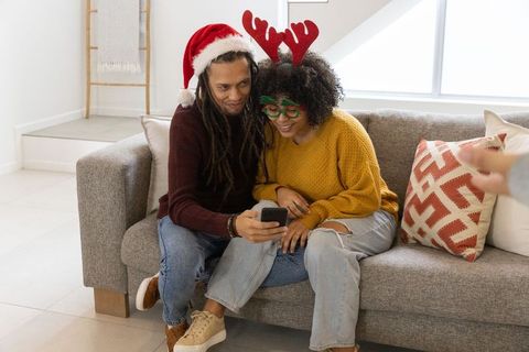 Couple wearing santa hat and reindeer antlers sharing smartphone on sofa