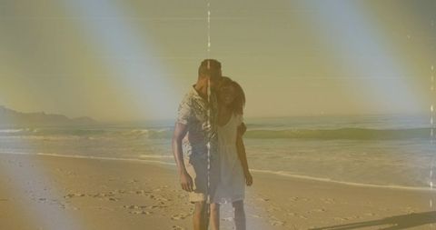 Couple walking along sunlit beach at golden hour with vintage film scratches and grain