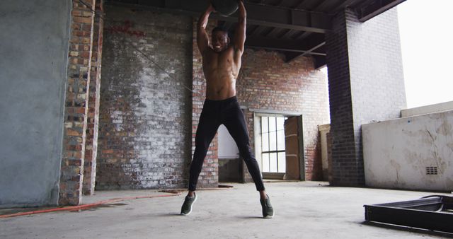Shirtless african american man exercising with medicine ball in an empty urban building. urban fitness and healthy lifetyle.