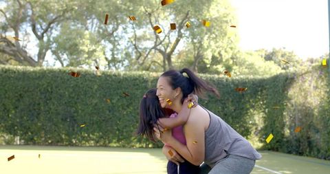 Joyful backyard embrace between mother and daughter with falling confetti and sunlight