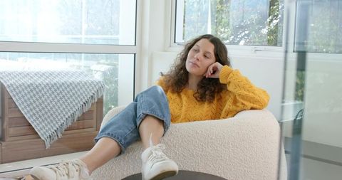 Serene woman reclining in sunlit lounge wearing mustard sweater, jeans and sneakers