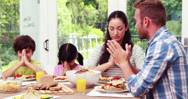 Family praying before eating lunch at home