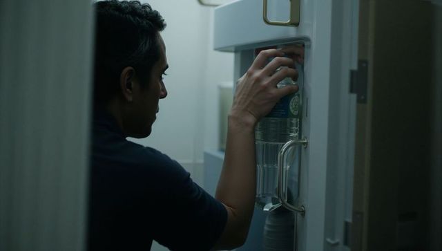 Man grabbing water bottle from refrigerator in dim compact kitchen