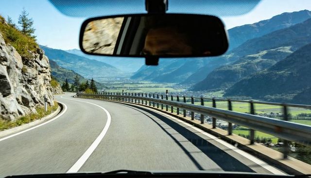 Driving through mountain pass on winding road from car interior with rearview mirror reflection