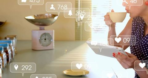 Woman sipping coffee using tablet with social notifications overlays in sunlit kitchen