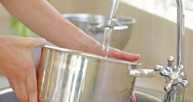 Woman filling pot with water from the tap at home in the kitchen