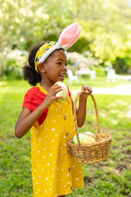 African american girl in bunny ears carrying easter eggs and basket in backyard. unaltered, easter day, celebration, childhood, cultures and holiday concept.