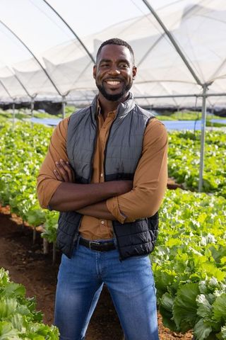 African American Farmer Smiling in Eco-Friendly Greenhouse with Lettuce