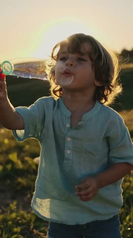 Boy Blowing Bubbles at Sunset in Field Vertical Video for Playful Family Moments