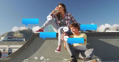 Young couple sharing messages on urban rooftop skate ramp with smartphones and earbuds