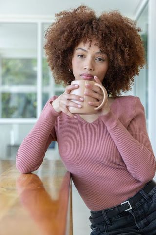 African american woman leaning on wooden counter holding mug, morning coffee portrait