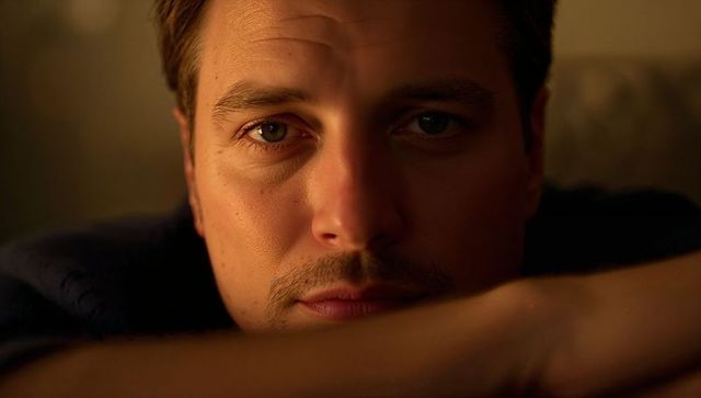 Intimate golden-hour portrait of man resting on forearms and gazing into camera