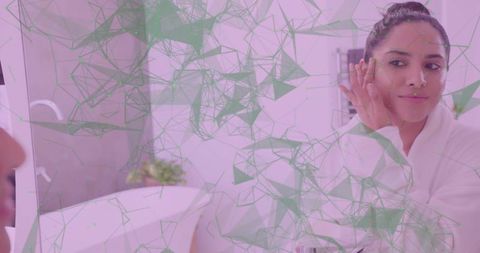 Indian woman applying face cream at bathroom mirror wearing white robe skincare ritual