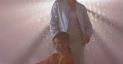 Serene asian duo posing on pastel pink backdrop wearing satin blue and brown bomber jackets