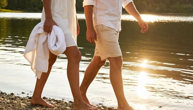 Couple walking barefoot along lakeshore at golden hour woman holding towel