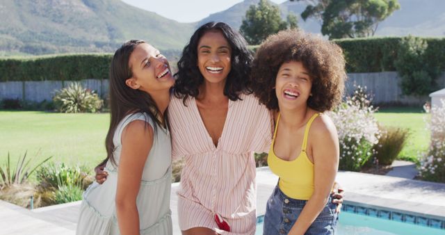 Three women enjoying a sunny day by the pool, laughing and having fun together. Perfect for advertisements promoting summer activities, vacation destinations, friendship, and leisure time. The background of mountains and green nature makes it ideal for lifestyle, travel, and outdoor-themed content.
