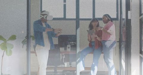 Team exploring virtual reality collaboration in glass-walled office with tablet and headset