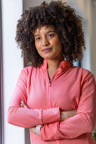 African american woman standing near bright window wearing coral pink jacket and smartwatch