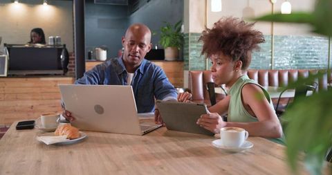 Colleagues collaborating over laptop and tablet in modern cafe with coffee and croissant
