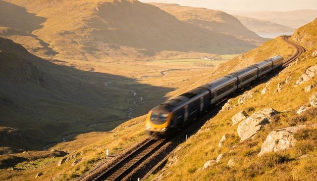 Traveling blue passenger train curving through golden highland valley in warm light
