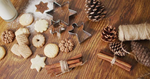 Baking holiday cookies with various shapes on wooden table, surrounded by pinecones and cinnamon sticks. Can be used for Christmas-themed food blogs, festive recipe cards, or holiday event promotions.