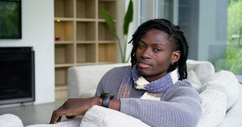 African american man relaxing on modern sofa wearing scarf and smartwatch