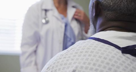 Doctor consulting senior patient in hospital gown during clinical examination with stethoscope