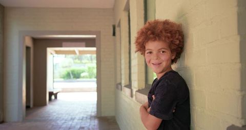 Smiling african teen leaning against green brick corridor wall with sunlight