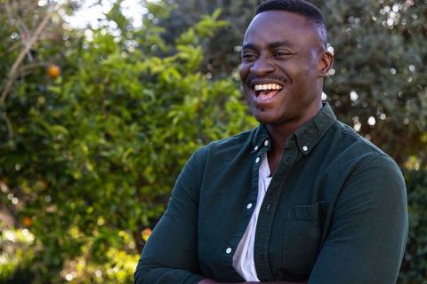 Joyful african american man laughing in backyard garden wearing earpiece and green shirt