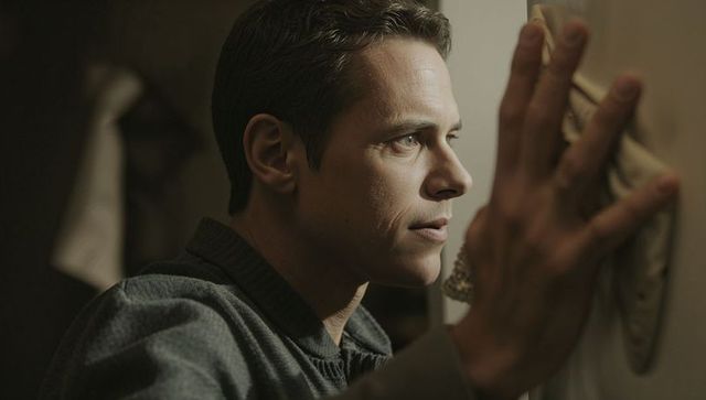 Contemplative light-skinned man wiping door with cloth, side-lit closeup domestic chore