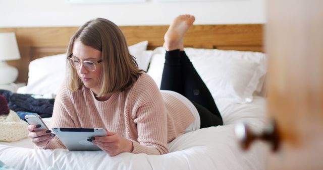 Woman using digital tablet and mobile phone in bedroom at home