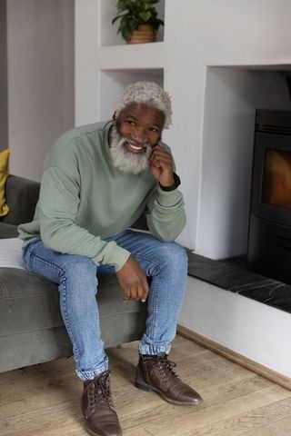 Senior african american man smiling sitting on sofa near fireplace in cozy modern room