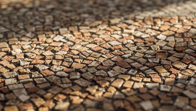Sunlit mosaic cobblestone pavement showcasing warm tesserae, earthy tones and textured grout