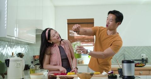 Couple cooking together in modern kitchen laughing while blending green smoothie