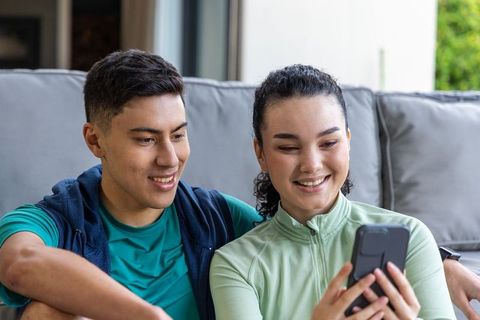 Young couple relaxing on sofa sharing smartphone and smiling together at home