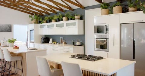 Modern open-plan kitchen with quartz island, gas cooktop, timber beams and greenery