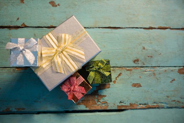 Colorful wrapped gifts with shiny bows and ribbons placed on a rustic wooden plank. Ideal for holiday-themed promotions, Christmas cards, festive advertisements, and celebration invitations.