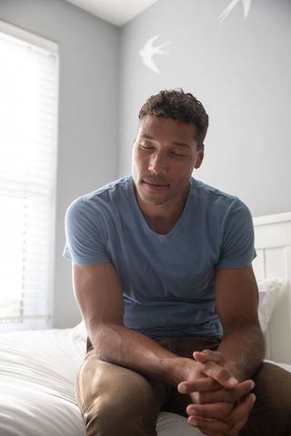 Contemplative man sitting on bed in serene minimalist bedroom