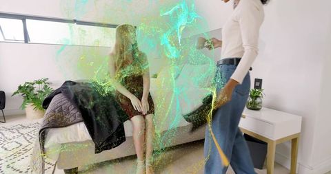 Woman sitting on bed talking with friend amid holographic green-blue particle cloud