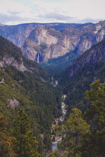Beautiful mountainous landscape featuring a flowing river through a dense forest valley, highlighting a majestic waterfall in the distance. Perfect for advertisements related to outdoor adventures, nature exploration, travel experiences, and holiday destinations.