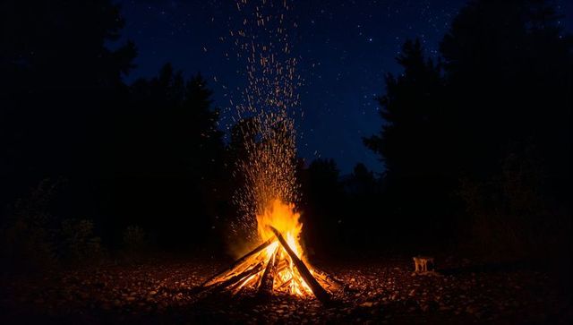 Bonfire sending golden sparks into starry night sky over glowing pebble ground