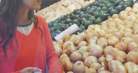 Young woman examining label while shopping produce at supermarket onion and avocado stand