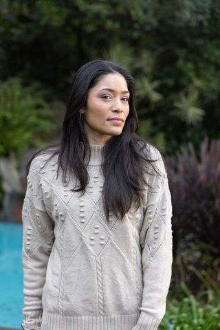 Woman standing poolside in backyard wearing beige knit sweater and hoop earrings