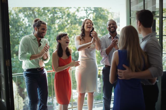 Group of friends applauding a couple during a party on a balcony. Perfect for use in content related to celebrations, social gatherings, friendship, and joyful moments. Ideal for promoting events, party planning, and lifestyle blogs.