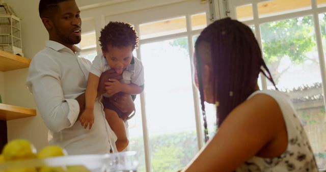 Front view of young black father holding his son and talking with mother in kitchen at home - Download Free Stock Photos Pikwizard.com