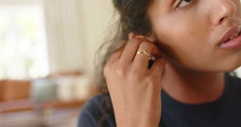 African american woman adjusting earring wearing thin gold ring in home closeup portrait