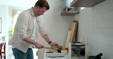 Adult man slicing multigrain bread in minimalist kitchen