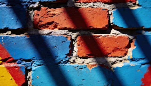 Sunlit weathered brick wall with vibrant blue paint and diagonal shadows